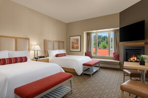 A hotel room with two beds, a TV, a fireplace, and a window with a view of trees.
