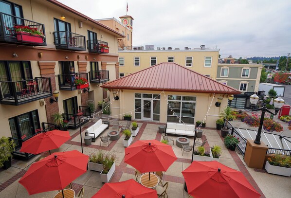A courtyard with outdoor seating, red umbrellas, and potted plants. - Inn at the 5th (Eugene)