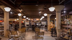 An indoor café with wooden tables and chairs, a bar area, and shelves stocked with bottles. - Inn at the 5th (Eugene)