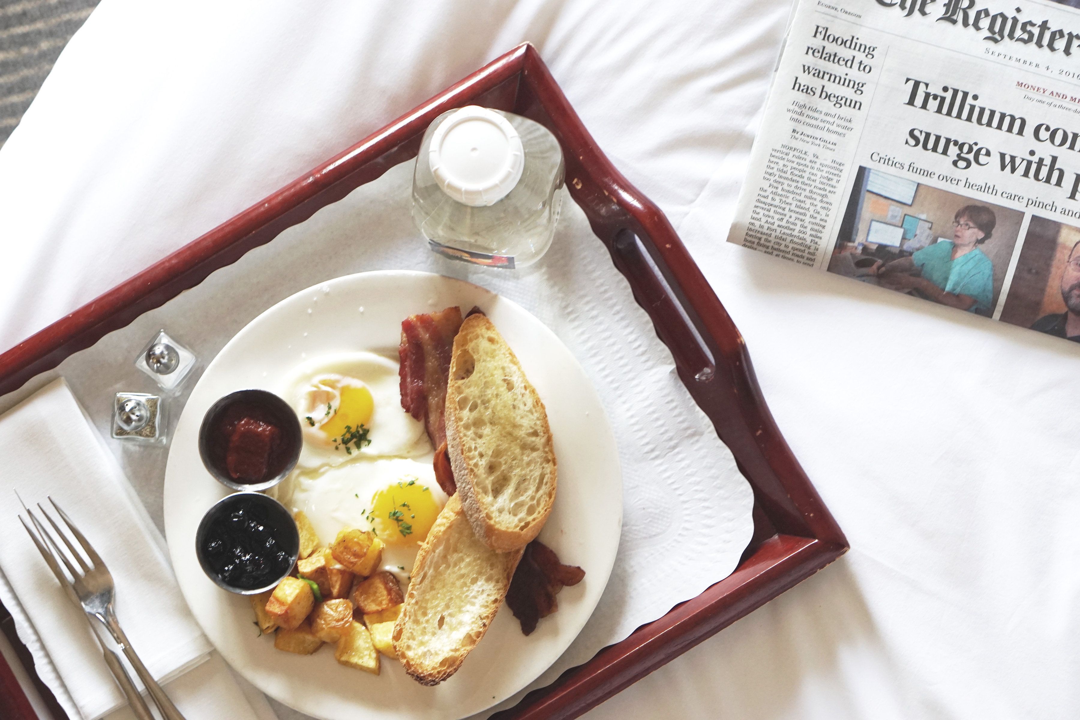 A tray with breakfast items including toast, eggs, and potatoes, alongside a newspaper.