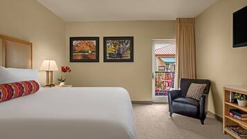 A hotel room with a large bed, a chair, a bookshelf, and two framed pictures on the wall.