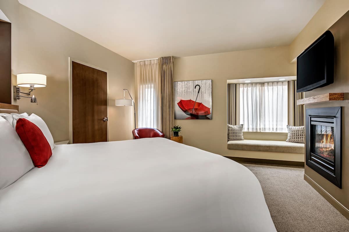 A hotel room with a large bed, a television, a fireplace, and a window with curtains.