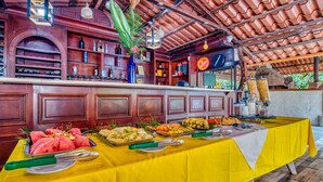 Una mesa de buffet con diversos alimentos y una zona de bar con estantes llenos de botellas y un reloj.