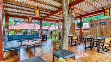 Un espace extérieur aménagé avec des tables et des bancs en bois, entouré d’une clôture en bois rustique et d’un grand arbre.