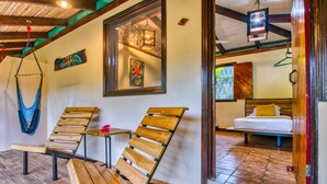 Una habitación con una hamaca, sillas de madera, una cama con almohada amarilla y un cuadro en la pared.