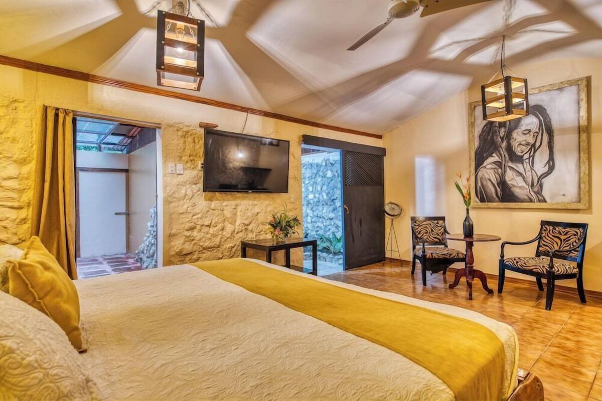 Een slaapkamer met een bed, een televisie, een tafel met stoelen en een schilderij aan de muur.