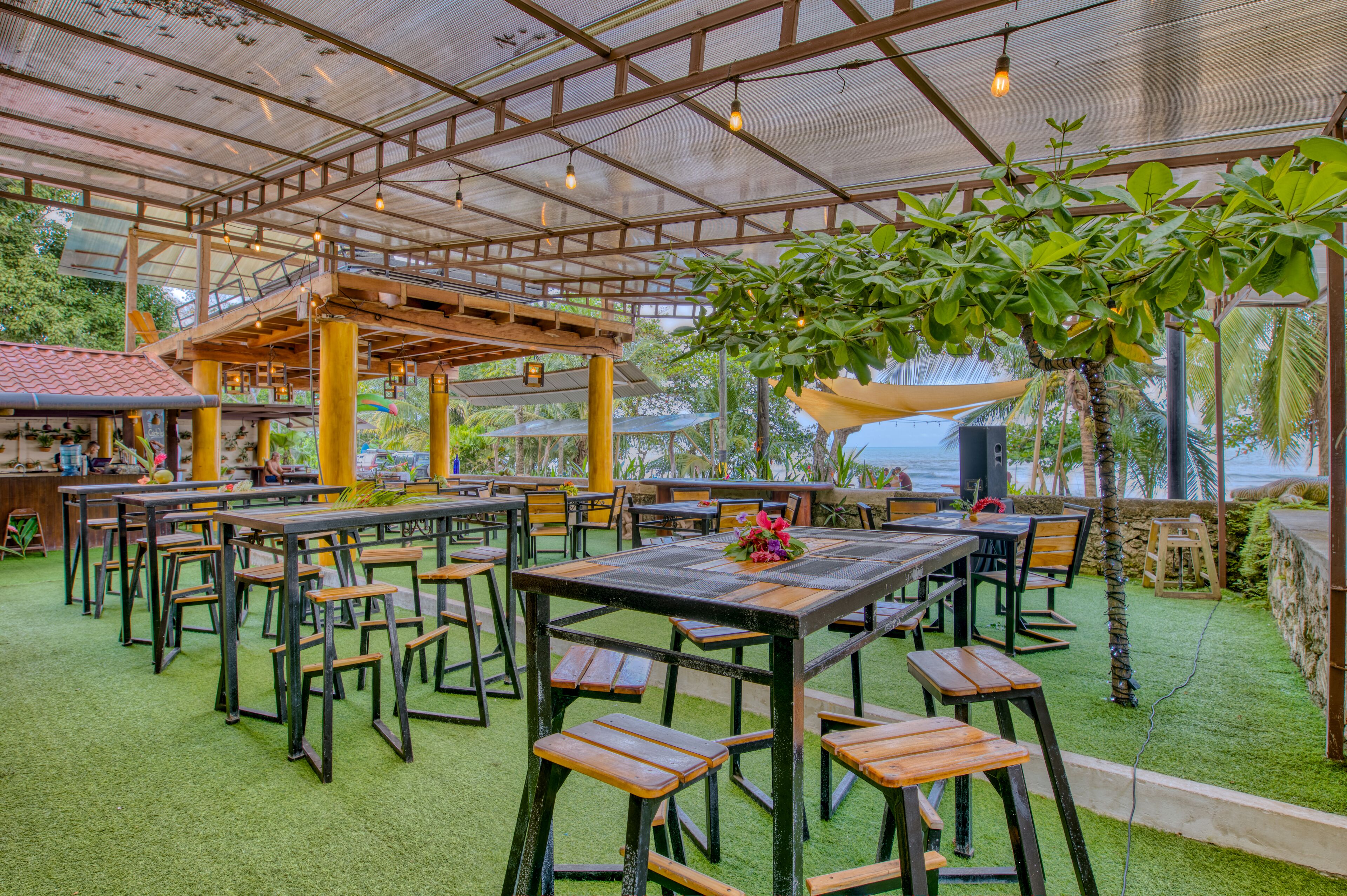 Une terrasse extérieure avec des tables et des chaises en bois, entourée de verdure et abritée par une structure à toit de verre.