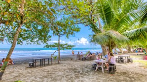 Un café frente al mar con terraza, palmeras y vista al océano.