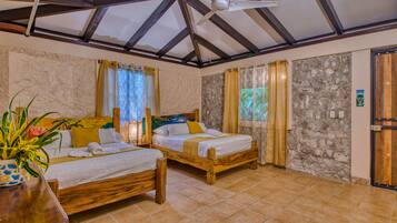 Una habitación con dos camas de madera, un ventilador de techo, paredes de piedra y una puerta de madera.