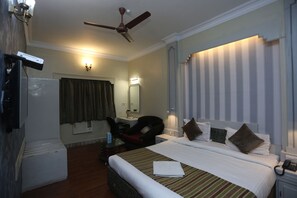 A hotel room with a bed, a desk, a chair, a television, and a ceiling fan. - Hotel Rushabh Home (Kolkata)
