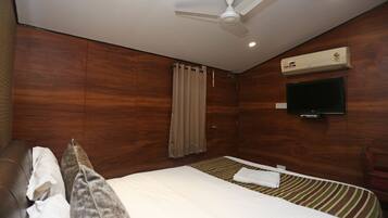 Habitación de hotel con cama, ventilador de techo, unidad de aire acondicionado, televisor y pared de madera.