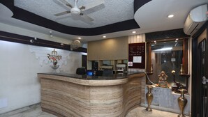 A reception area with a curved marble counter, ceiling fan, wall-mounted air conditioning, and a decorative statue. - Hotel Rushabh Home (Kolkata)