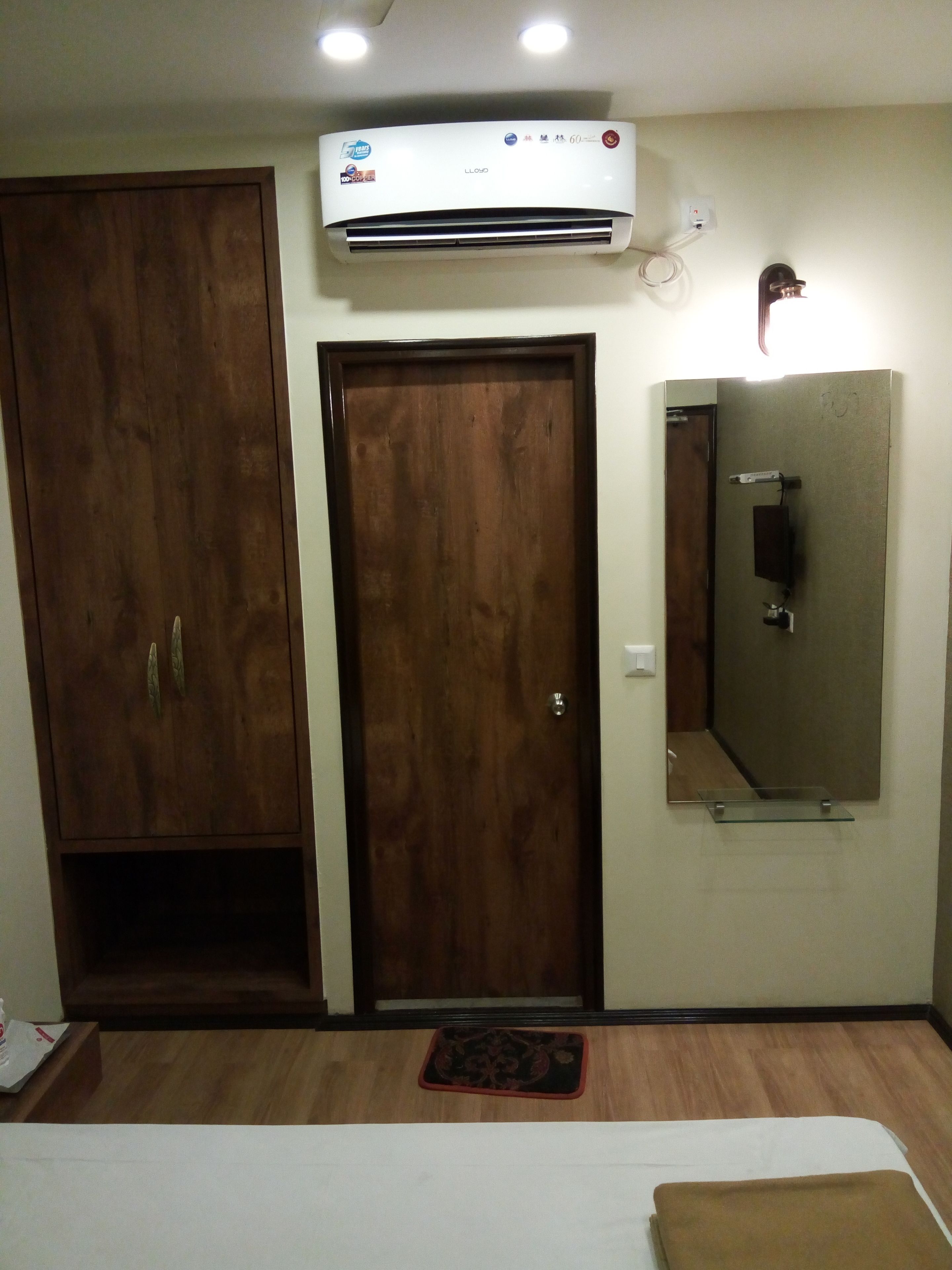 A hotel room with a wooden wardrobe, a door, a mirror, and an air conditioning unit.