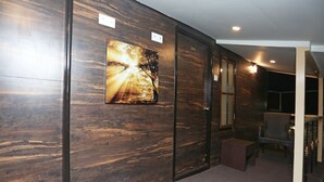 A hallway with a wooden wall, a framed picture, a door, and a small table with a chair. - Hotel Rushabh Home (Kolkata)