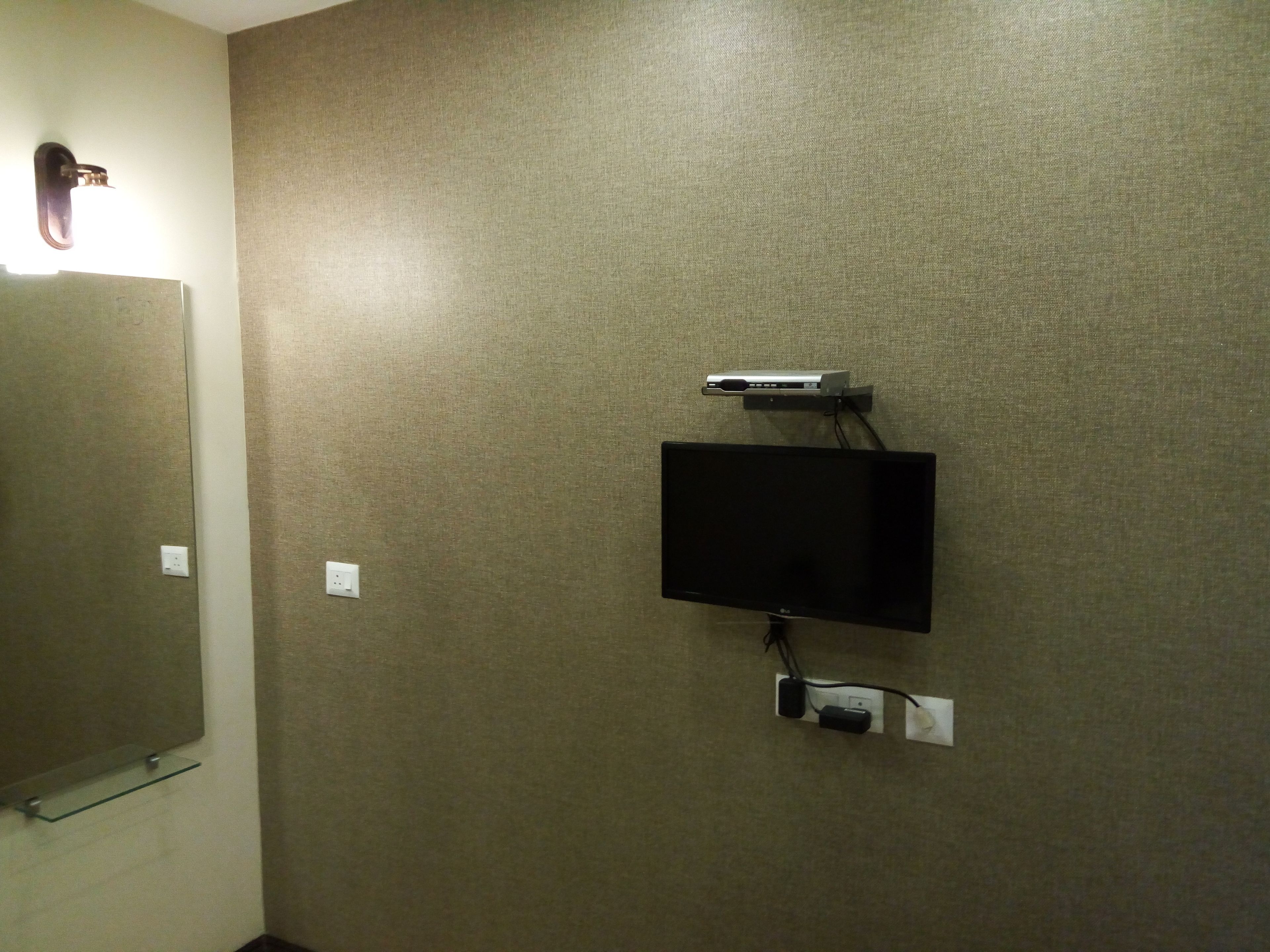 A wall-mounted television and a small shelf with a mirror.