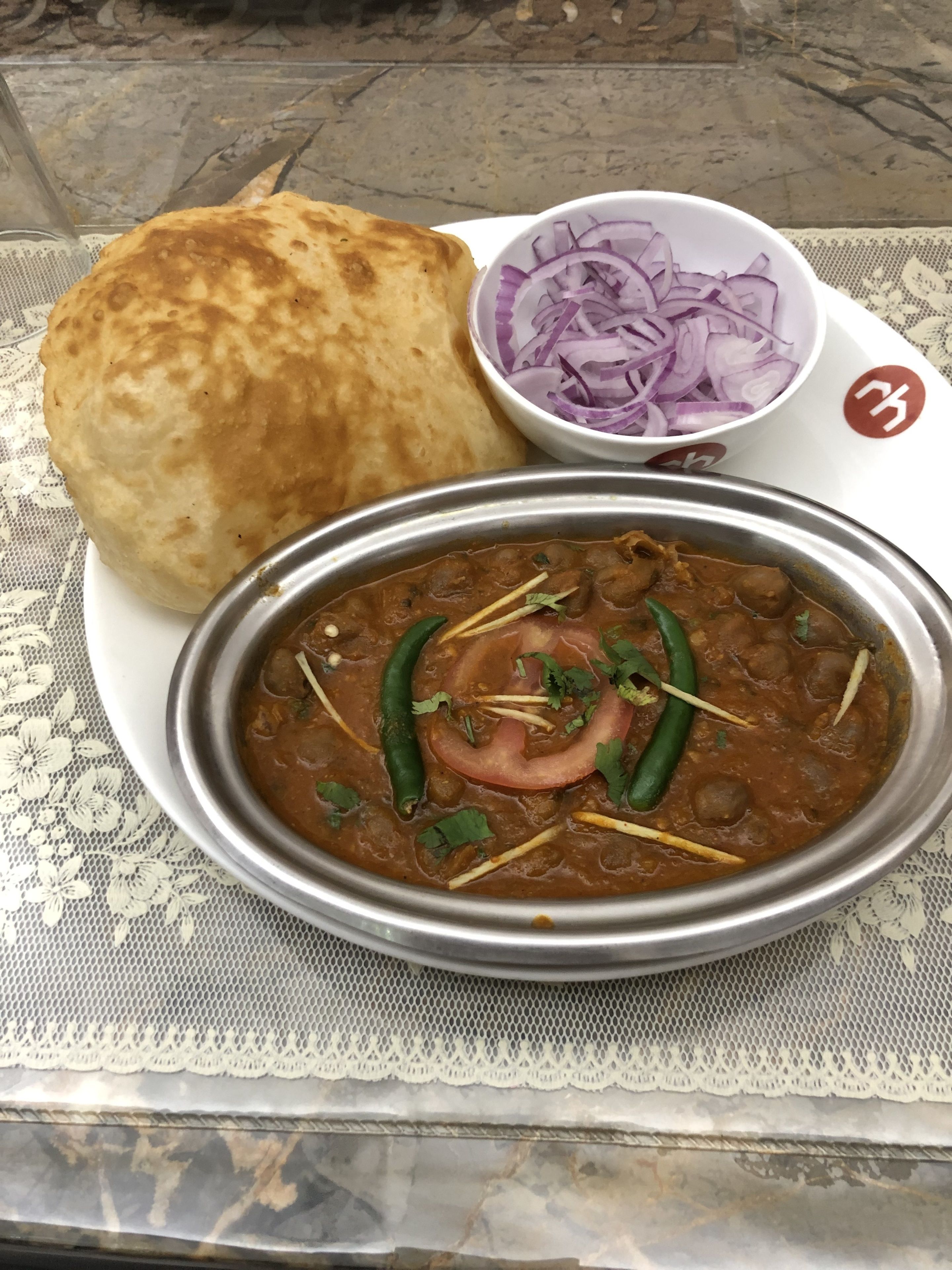 A meal consisting of a bread roll, sliced onions, and a bowl of curry with green chilies and herbs.
