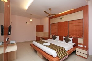 A modern hotel room with a large bed, a desk, a chair, a ceiling fan, and a TV. - Hotel Rushabh Home (Kolkata)