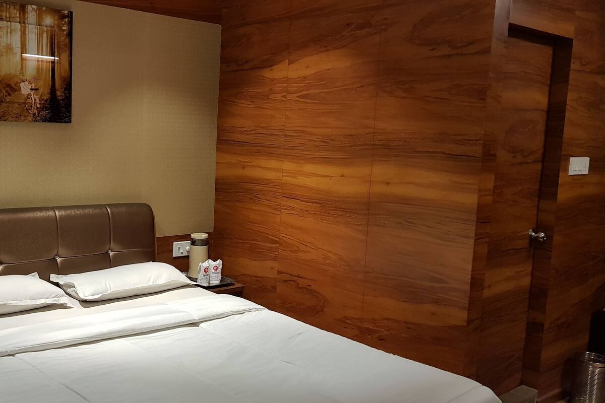 A neatly made bed with white linens, a brown upholstered headboard, and a wall-mounted painting of a forest scene.