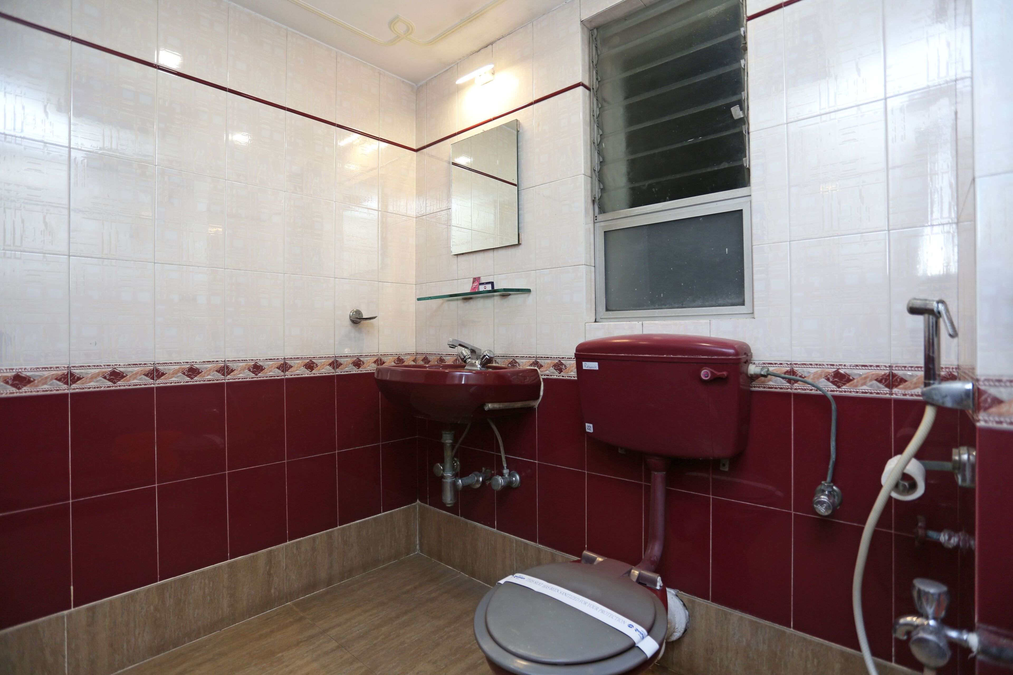 A bathroom with a toilet, sink, mirror, and window.