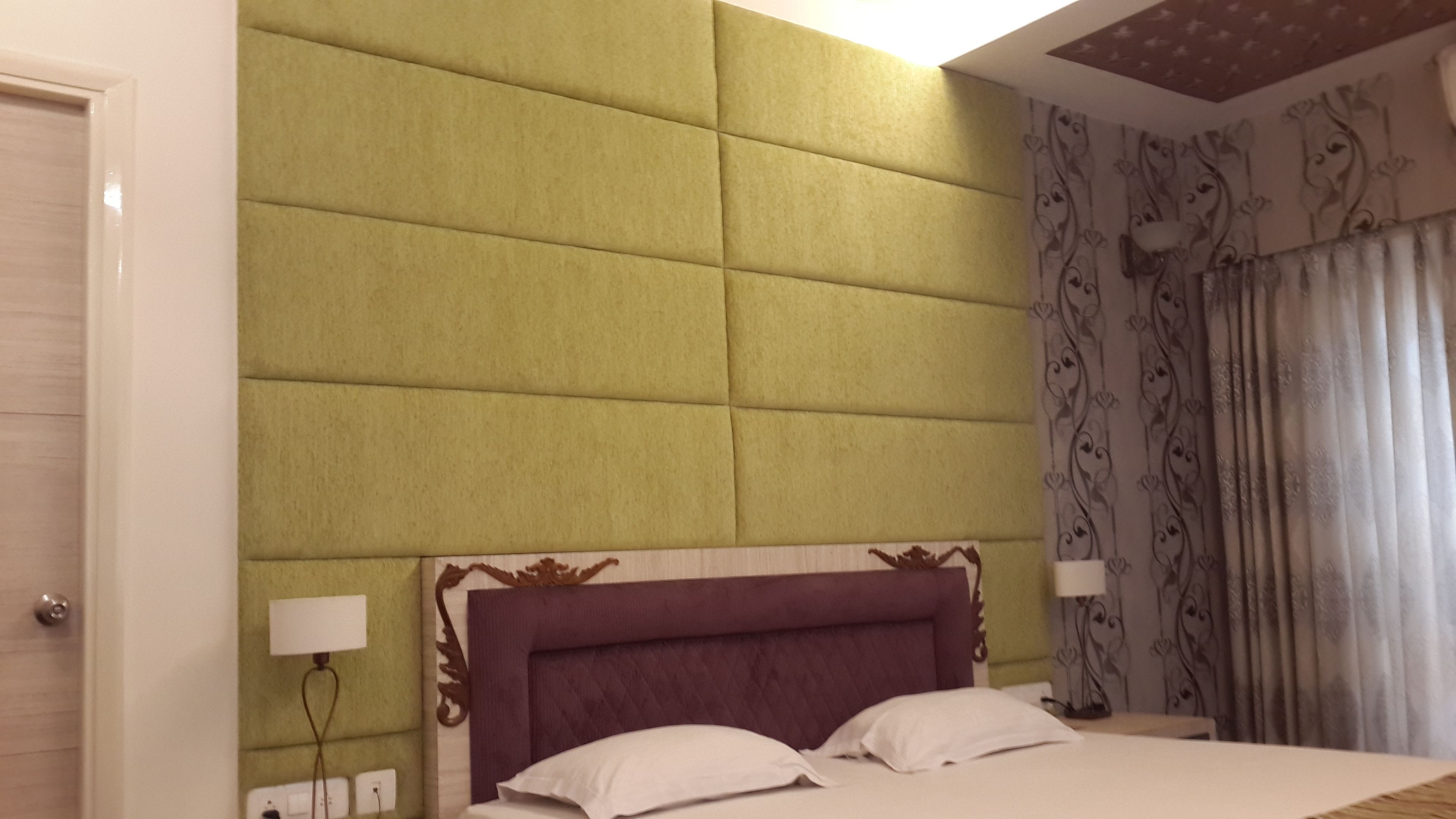 Habitació d'hotel amb un llit gran, un panell de capçalera amb folradura verda i cortines estampades.