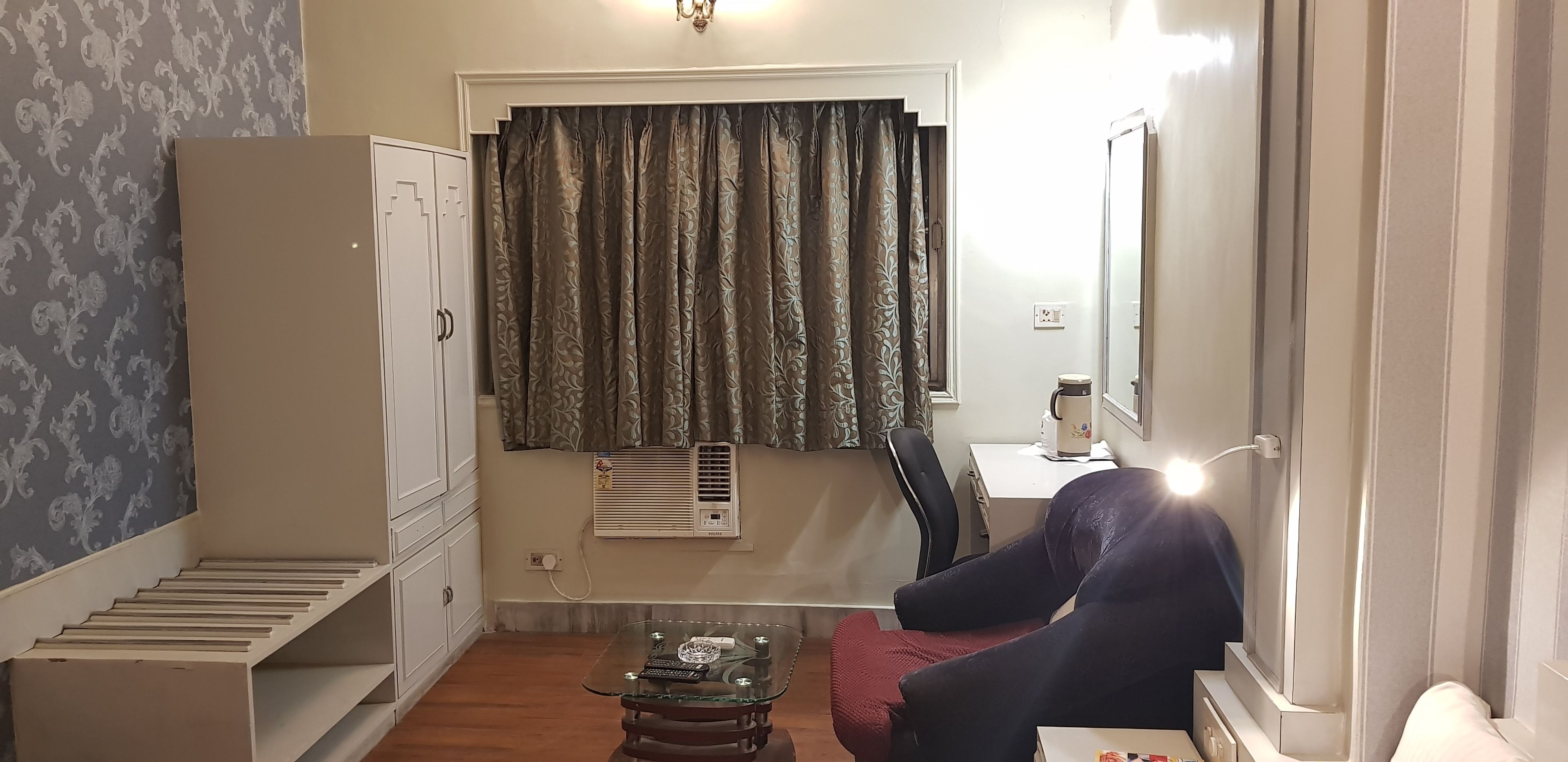 Una habitación compacta con cama, una mesita, una silla, un armario y una ventana con cortinas.