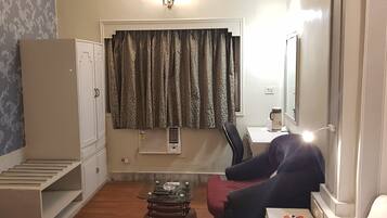 Una habitación compacta con cama, una mesita, una silla, un armario y una ventana con cortinas.