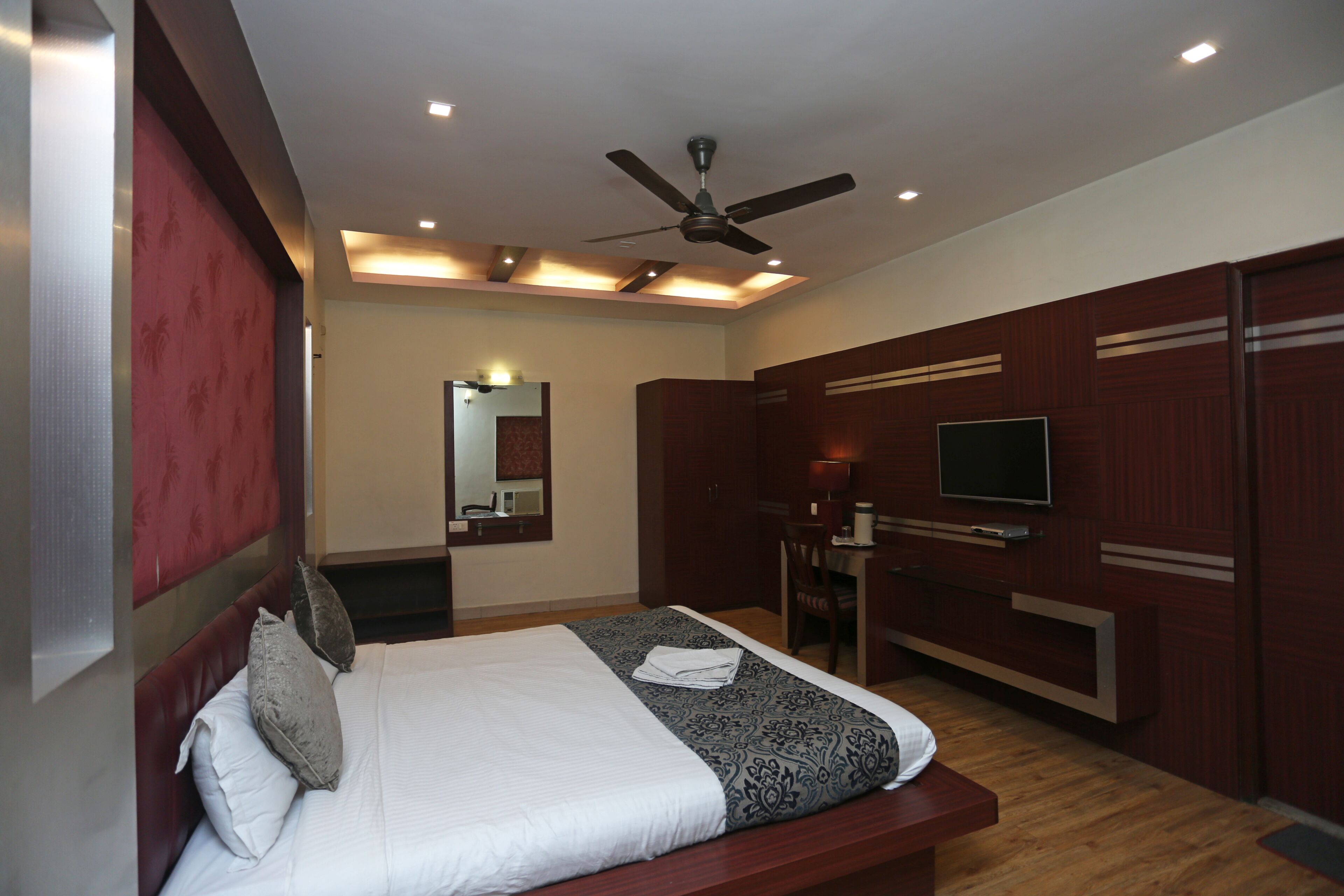Une chambre d’hôtel moderne dotée d’un grand lit, d’un ventilateur de plafond, d’une télévision et d’un bureau avec une chaise.