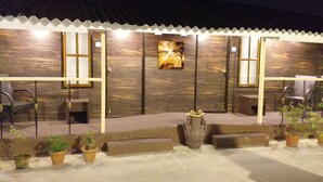 A covered outdoor seating area with a wooden wall, a bench, and potted plants. - Hotel Rushabh Home (Kolkata)