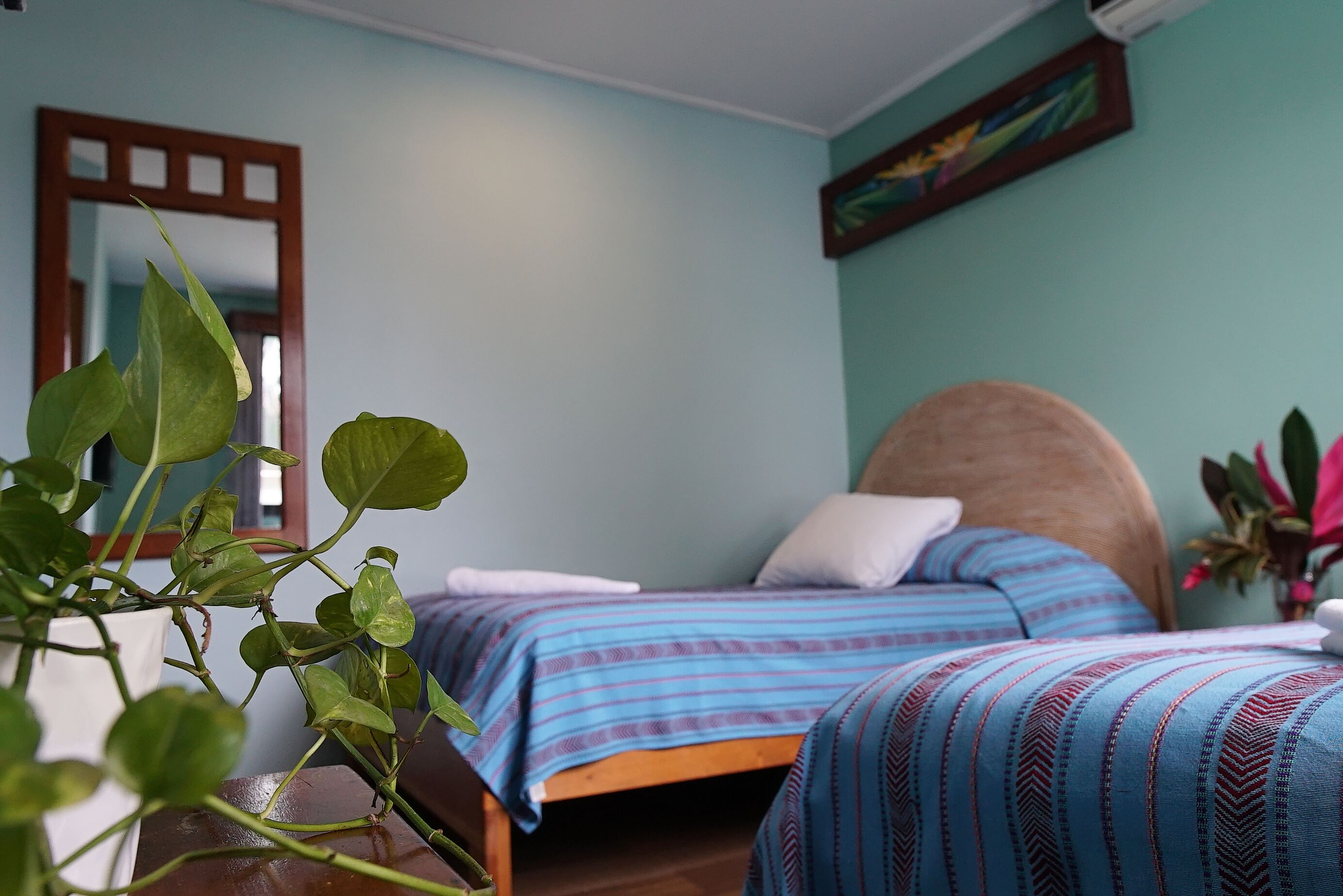A bedroom with two beds, a mirror, a painting, and a potted plant.