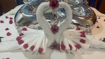 A table with a decorative centerpiece featuring swan-shaped towels and rose petals, surrounded by silver balloons.