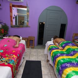 Two beds are covered with patterned bedspreads in this cozy room featuring a mirror and shelf.