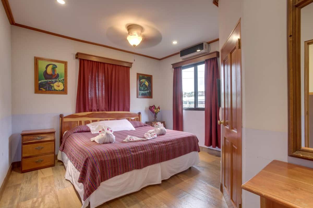 A bedroom with a wooden bed, red curtains, a nightstand, and two wall-mounted paintings.
