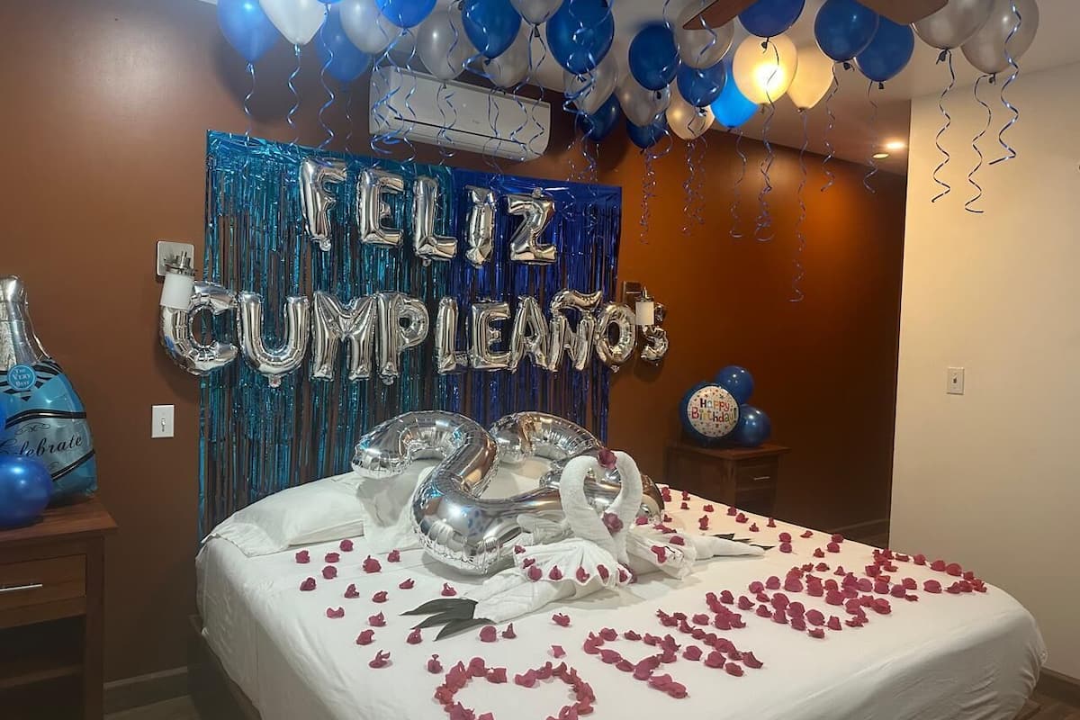 A room decorated for a birthday celebration with balloons, a cake, and a banner that reads "Feliz Cumpleaños".