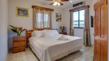 Un dormitorio con cama, mesita de noche, ventilador de techo y ventana con cortinas.