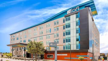 Un moderno edificio de hotel con un llamativo letrero 'aloft', que presenta una fachada mixta de vidrio y ladrillo, y un diseño de techo plano.