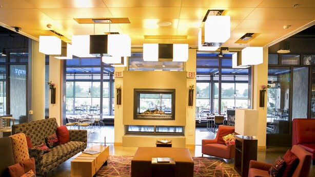 Een moderne lobby met een gestreept bankje, rode fauteuils, een bijzettafeltje en een open haard.