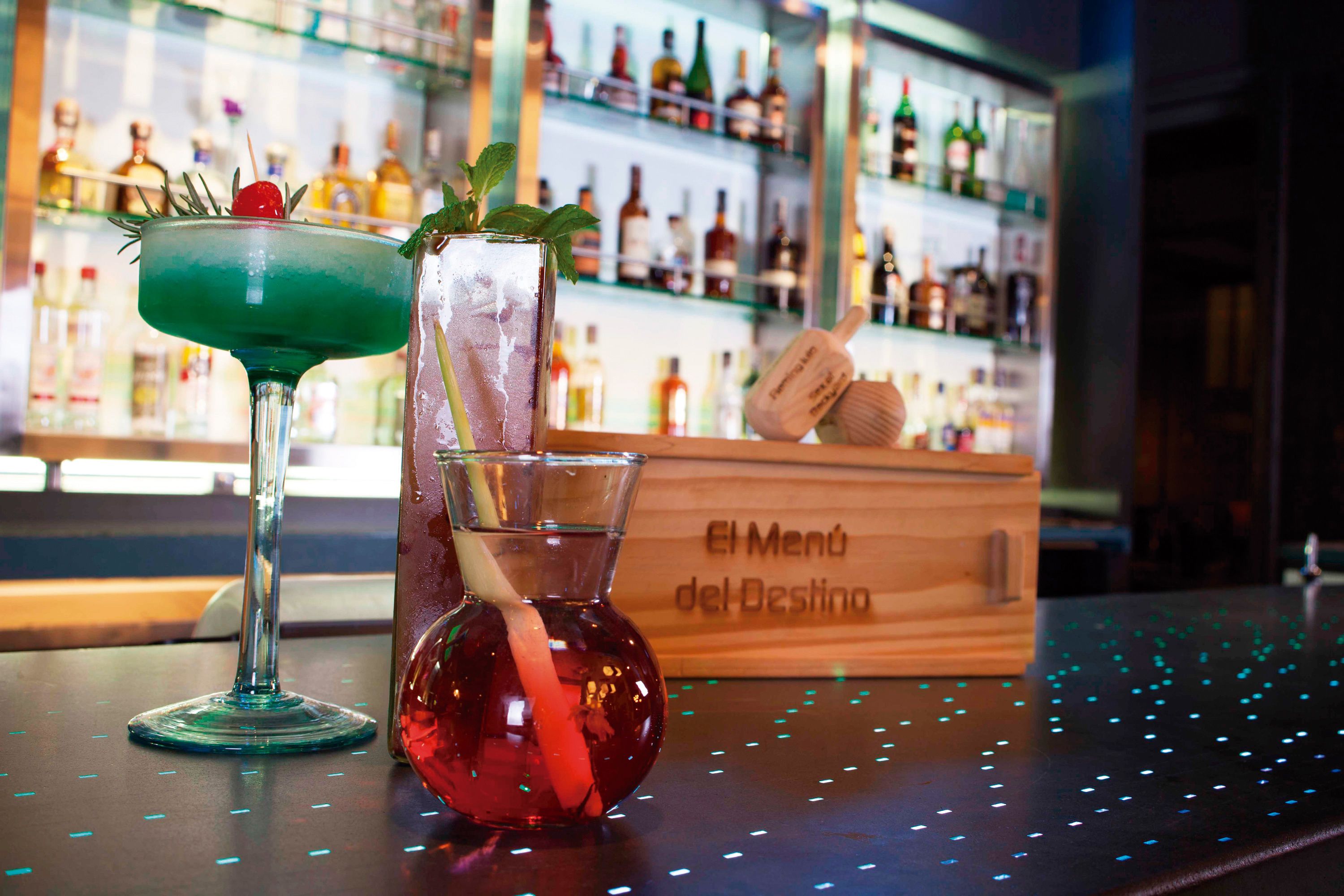 Two cocktails on a bar counter with a background of shelves stocked with bottles.