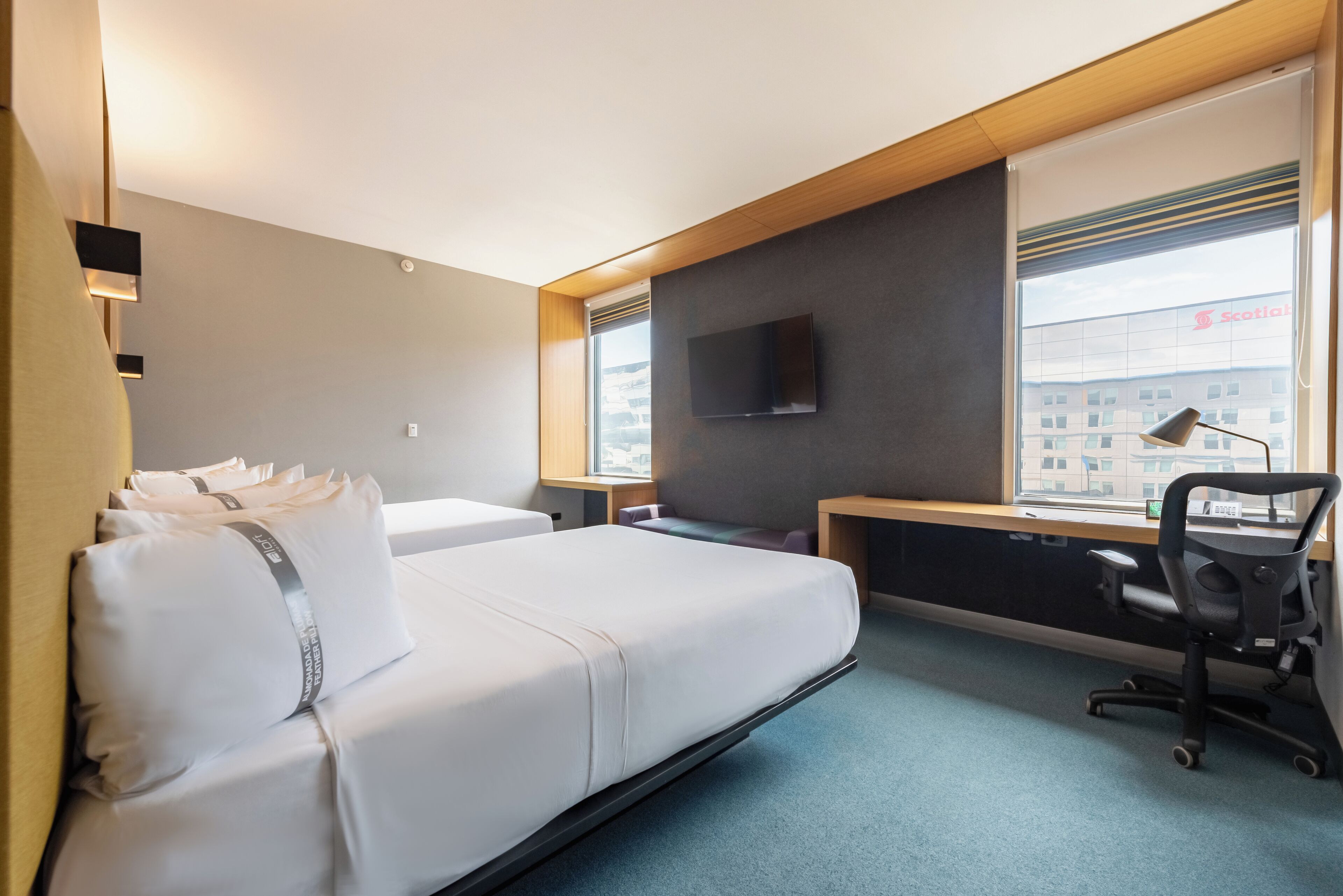 Una habitación de hotel con cama, escritorio, silla, televisor y ventana con persianas.