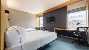 Una habitación de hotel con cama, escritorio, silla, televisor y ventana con persianas.