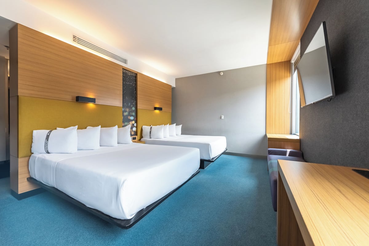 A hotel room with two beds, a desk, a flat-screen TV, and a large window.