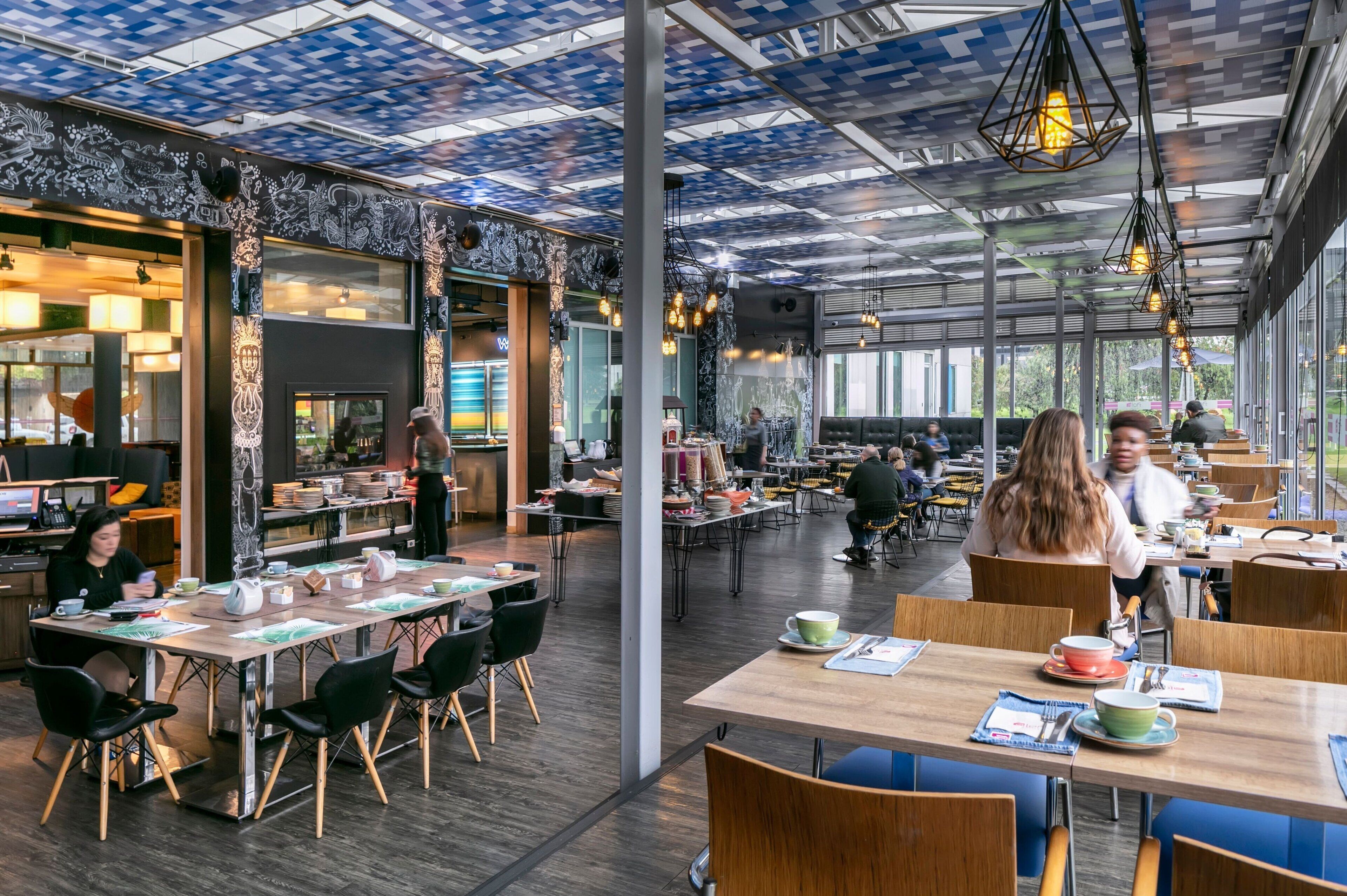 A spacious café with high tables and chairs, large windows, and a patterned ceiling.