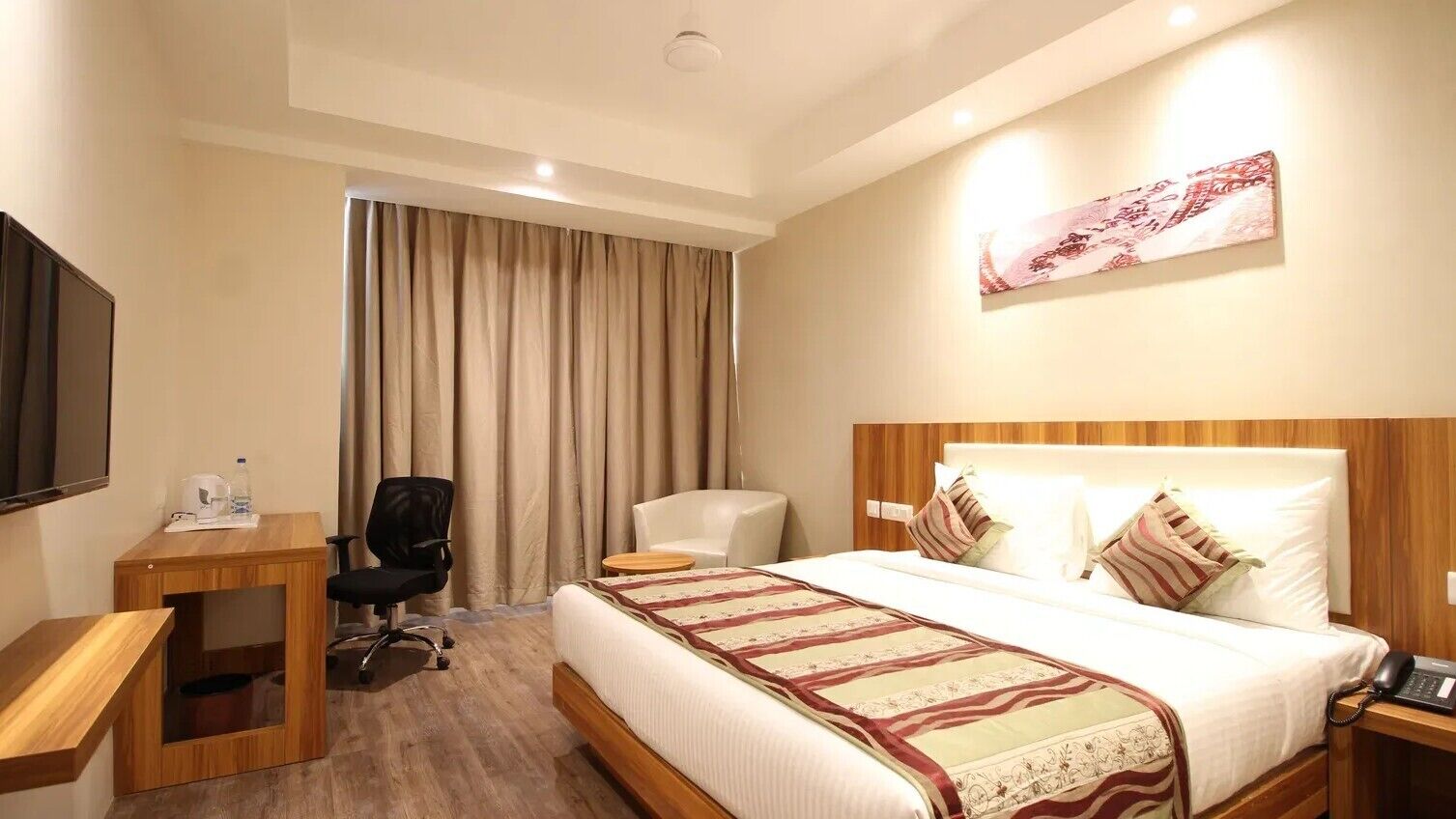 Ein Hotelzimmer mit einem Bett, einem Schreibtisch, einem Sessel, einem Fernseher und einem Vorhang.