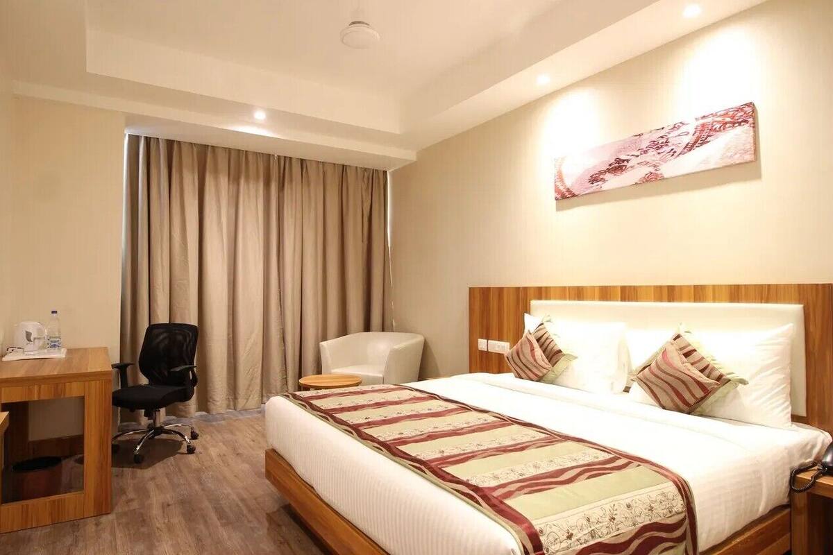 Una habitación de hotel con cama, escritorio, silla, televisor y cortina.