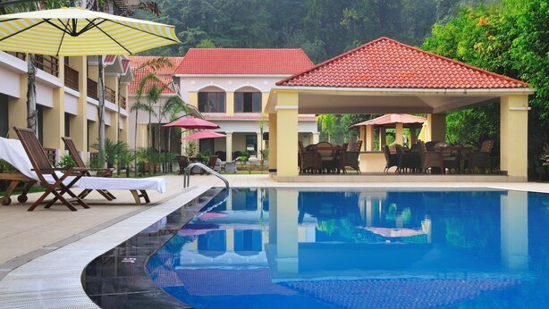 Ein Pool mit Liegestühlen und Sonnenschirmen, eine überdachte Sitzgruppe und ein Gebäude mit roten Ziegeldach.