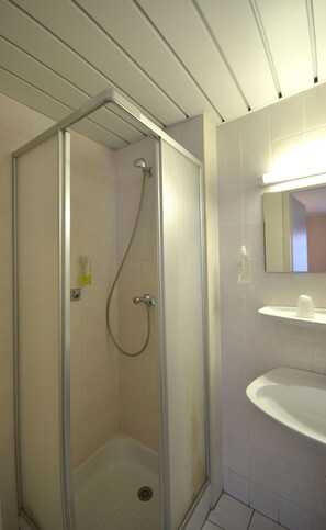 Ducha con puerta de cristal, lavamanos con espejo y lámpara sobre el espejo.