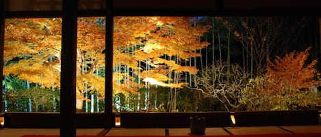 A traditional Japanese room with tatami flooring, a low table, and a view of autumn trees through a window.