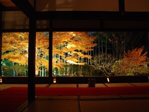 Una habitación japonesa tradicional con suelo de tatami, una mesa baja y vistas a árboles otoñales por una ventana.