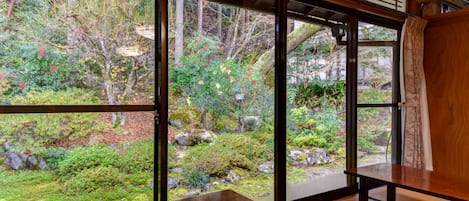 A room with a wooden table and bench, large sliding glass doors leading to a garden with rocks and greenery.