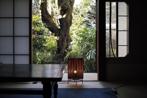 A traditional Japanese room with tatami flooring, a low table, and a view of a large tree through a sliding door. - Japanese Inn Yoshimizu (Kyoto)