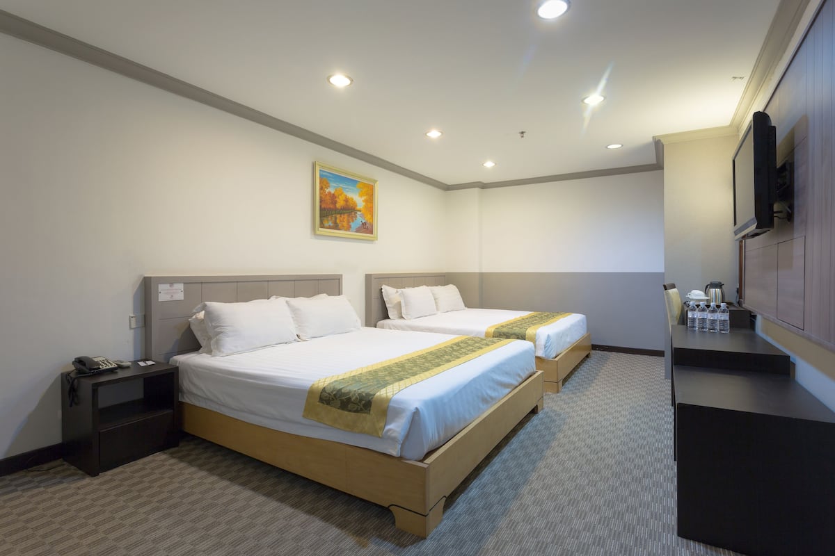 A hotel room with two beds, a desk, a chair, a TV, and a painting on the wall.